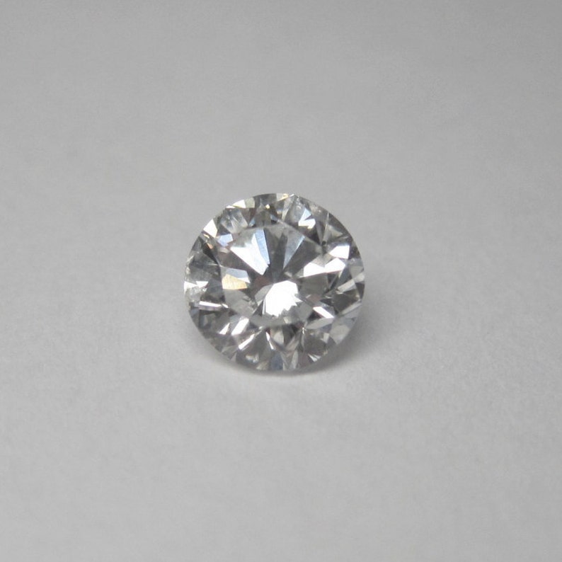 May include: A round, clear diamond gemstone with many facets.