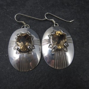 May include: A pair of silver earrings with oval-shaped settings featuring a brown gemstone. The earrings have a geometric design with a starburst pattern.