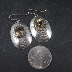 May include: A pair of silver earrings with oval-shaped settings featuring a brown gemstone. The earrings have a geometric design with radiating lines.