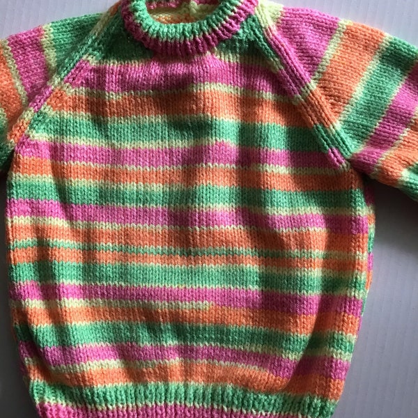 This girls' jumper/sweater fits a 20 inch chest or a 9 month - 18 month old. It is knitted in striped yarn in pink, orange,green and lemon.