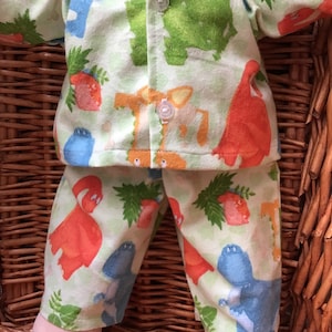 May include: Green and orange pyjamas with a dinosaur print. The pyjamas have a button-up shirt and long trousers.