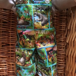 May include: A pair of blue dungarees with a jungle scene print featuring characters from Disney's The Jungle Book. The dungarees have two silver buttons on the straps.