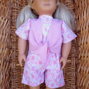 May include: A doll wearing a pink and white gingham vest and matching shorts with a floral print. The doll has blonde hair and blue eyes.