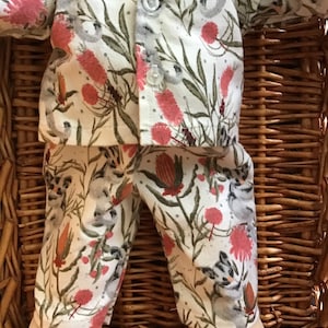 May include: A white pajama set with a floral print featuring grey possums, green leaves, and pink flowers. The pajamas are made of soft cotton and are perfect for a cozy night in.