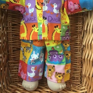 May include: A colourful doll's pyjamas set with a variety of animal prints, including giraffes, ducks, zebras, and a boat. The pyjamas are made of soft fabric and are perfect for a child's doll.