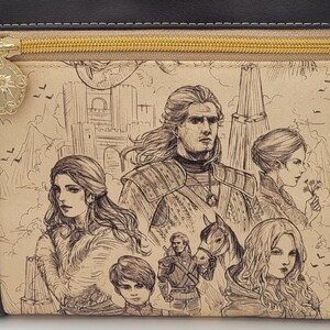 May include: A black leather zippered pouch with a beige fabric lining featuring a hand-drawn illustration of a group of people in a medieval setting. The illustration includes a man with a sword, a woman with long hair, a young boy, and a horse.