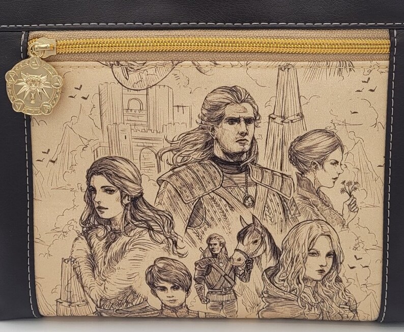 May include: A black leather zippered pouch with a beige fabric lining featuring a hand-drawn illustration of a group of people in a medieval setting. The illustration includes a man with a sword, a woman with long hair, a young boy, and a horse.