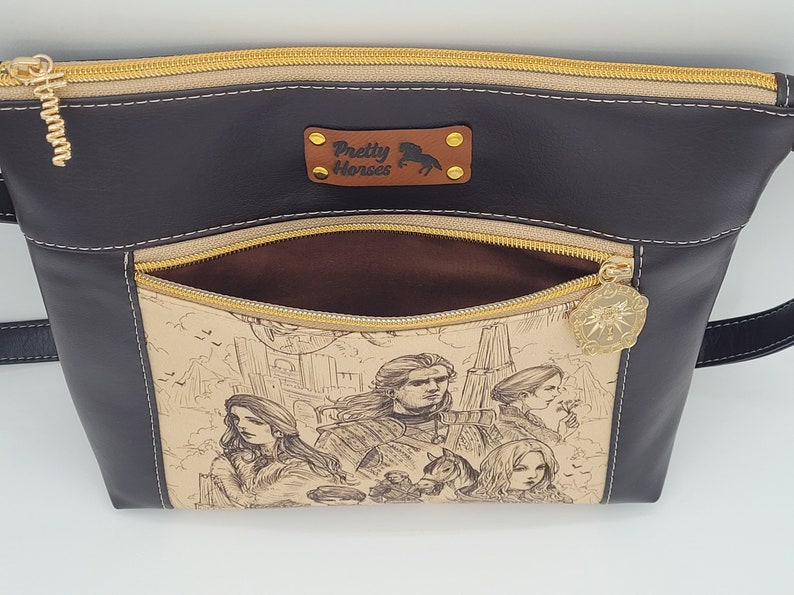 May include: A black leather purse with a gold zipper and a brown fabric lining. The purse has a pocket on the front with a gold zipper and a gold charm. The pocket features a printed design of a city scene with people and buildings.