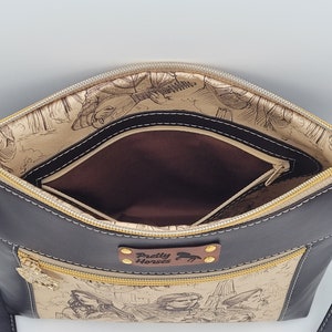 May include: Black leather crossbody bag with a gold zipper and a brown fabric lining. The bag has a small pocket on the front with the text "Pretty Horses" and a horse illustration.