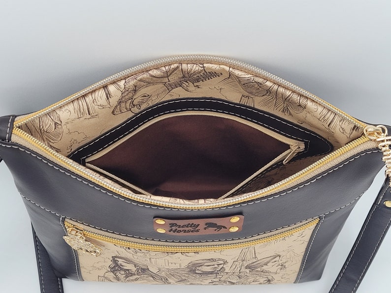 May include: Black leather crossbody bag with a gold zipper and a brown fabric lining. The bag has a small pocket on the front with the text "Pretty Horses" and a horse illustration.