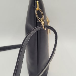 May include: A black crossbody bag with a gold zipper and a gold chain strap. The bag has a flap closure and a small pocket on the front.