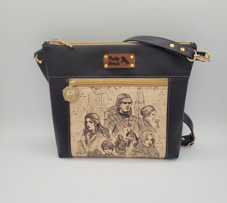 May include: Black crossbody bag with a gold zipper and a brown leather patch that says "Pretty Horses". The front of the bag features a black and white illustration of a group of people.