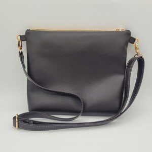 May include: A black leather crossbody bag with a gold zipper and a long adjustable strap.
