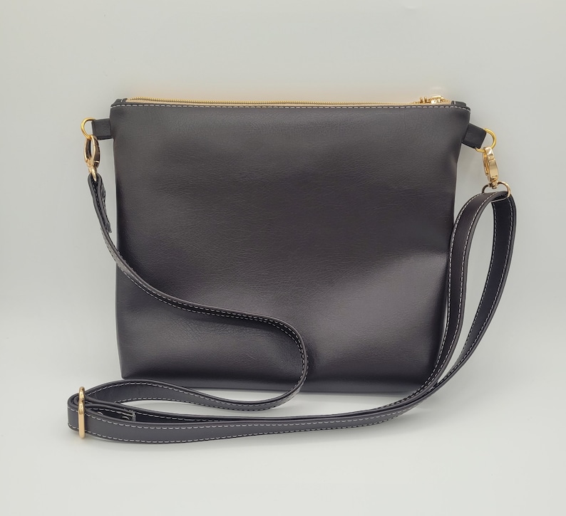 May include: A black leather crossbody bag with a gold zipper and a long adjustable strap.
