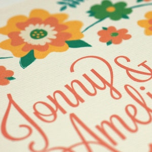 May include: A wedding invitation with a floral design in shades of orange, yellow, and green. The names "Jonny & Amelia" are written in a cursive font in a light pink color.