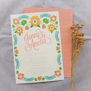 May include: A wedding invitation with a floral border in shades of pink, yellow, and green. The invitation reads "Jonny & Amelia" and includes the wedding date, time, and location. RSVP information is also included.