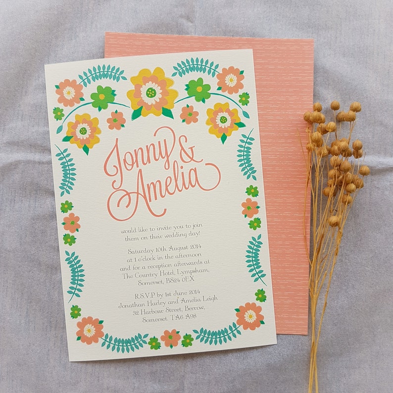May include: A wedding invitation with a floral border in shades of pink, yellow, and green. The invitation reads "Jonny & Amelia" and includes the wedding date, time, and location. RSVP information is also included.