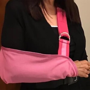 Puede incluir: Un cabestrillo rosa para el brazo con una correa para el hombro a juego. El cabestrillo est&aacute; dise&ntilde;ado para sujetar el brazo y se asegura con un cintur&oacute;n negro. La correa para el hombro tiene un anillo en D de metal plateado.