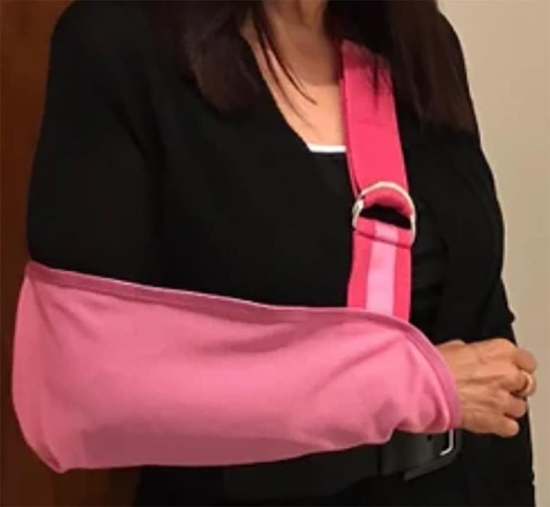 Puede incluir: Un cabestrillo rosa para el brazo con una correa para el hombro a juego. El cabestrillo est&aacute; dise&ntilde;ado para sujetar el brazo y se asegura con un cintur&oacute;n negro. La correa para el hombro tiene un anillo en D de metal plateado.