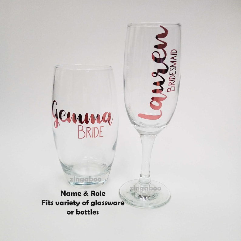 May include: Two clear glass champagne flutes with rose gold vinyl lettering. The larger flute says "Gemma Bride" and the smaller flute says "Lauren Bridesmaid".
