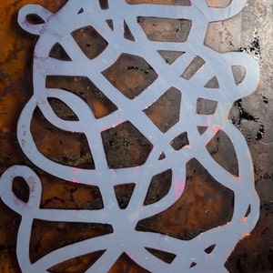 May include: A blue stencil with a geometric design on a brown background. The stencil is made of a thin, flexible material and has a smooth surface.