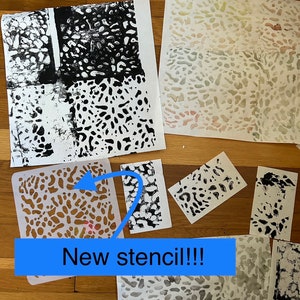 May include: A close-up of a new stencil with a black and white abstract pattern. The stencil is on a wooden surface with several pieces of paper with black ink prints of the same pattern. The text "New stencil!!!" is written on a blue rectangle.