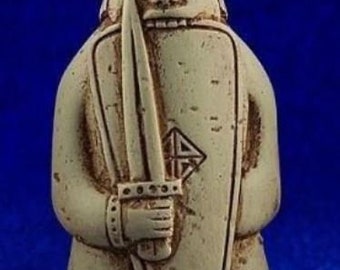 Puede incluir: Una figurita de cerámica beige de un guerrero sosteniendo una espada y un escudo. El guerrero lleva un casco y tiene una expresión severa. El escudo tiene un diseño de nudo celta.