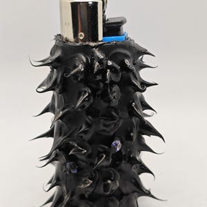 May include: A black lighter with a textured, spiky surface. The lighter has a silver top and a blue plastic piece on the side.