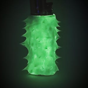 May include: A glowing green lighter with a textured, spiky exterior. The lighter's top is black, contrasting with the bright green body. The design gives the lighter a unique, eye-catching appearance.