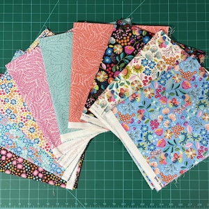 Puede incluir: Una colección de cuadrados de tela con varios patrones florales y botánicos. Las telas presentan colores como rosa, azul, coral y negro, con orillos blancos visibles. Los cuadrados están dispuestos sobre una esterilla de corte verde.