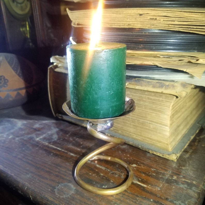 May include: A green candle with a flame burning on top of a gold metal candle holder. The candle holder is shaped like a spiral.