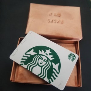 May include: A white gift card with the Starbucks logo, a green mermaid with a crown, and the text "Starbucks" in a small font. The gift card is in a copper box with the inscription "J & G 5.12.12".