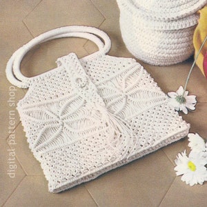 以下が含まれることがあります： 正方形の白いかぎ針編みハンドバッグ。丸みを帯びた2つのハンドルが付いています。バッグは詳細なパターンとフリンジのディテールが特徴です。「digital pattern shop」の文字がバッグの左側に縦に印刷されています。