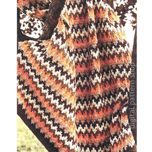 May include: A crocheted blanket with a chevron pattern in brown, orange, white and black colours. The blanket is draped over a tree branch.