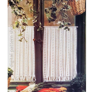 May include: Two white crocheted curtains hang in a window, with a fringe at the bottom. The curtains are made of a series of vertical lines with small holes. The window is framed by dark wood and has a basket of plants hanging above it.