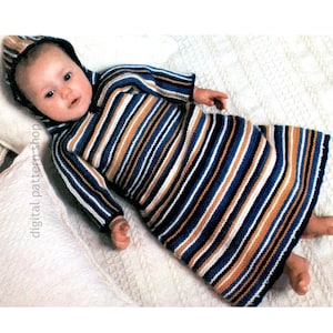 May include: A striped baby sleeping bag with a hood, knitted in blue, white, and brown yarn. The baby is wearing the sleeping bag and lying on a white blanket.