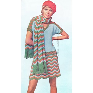 Puede incluir: Un conjunto de punto de ganchillo con un patrón de chevron en tonos de verde, naranja y azul. El conjunto incluye una blusa de manga corta y una falda a juego con ribete de flecos. La modelo lleva una boina roja.