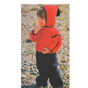 May include: A red knitted hooded sweater with black trim and matching blue knitted pants. The sweater has a pom-pom on the hood. The child is wearing the outfit outdoors.