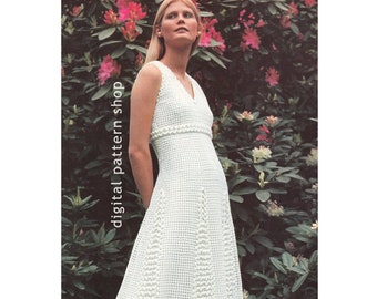 Puede incluir: Un vestido blanco de crochet con escote en V y un corpiño ajustado. El vestido tiene una falda acampanada y está decorado con un ribete de crochet alrededor del escote y la cintura. El vestido está fotografiado en una modelo de pie frente a un arbusto de flores rosas.