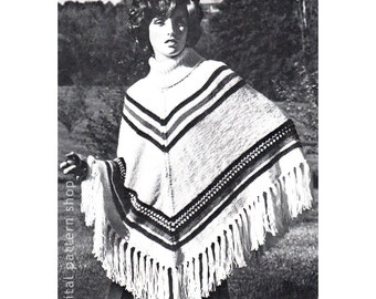 Op de afbeelding: Een zwart-witfoto van een vrouw die een witte gebreide poncho draagt met zwarte en rode strepen en een franje rand. De poncho wordt gedragen over een trui met een rolkraag.
