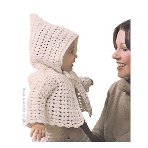 May include: A baby wearing a white, open-weave crochet hooded jacket and matching scarf. The jacket has long sleeves and a scalloped hem. The baby is being held by a person wearing a brown turtleneck. The words "digital pattern shop" are printed vertically on the left side.