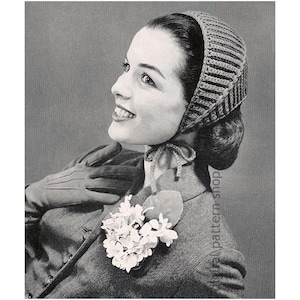 Può includere: Fotografia vintage in bianco e nero di una donna con un copricapo lavorato a maglia a righe orizzontali. Indossa anche una giacca grigia, guanti e una spilla floreale. La donna sorride e guarda in alto.