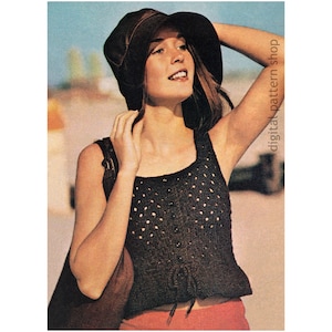 May include: A crochet top with a square neckline and a tie at the bottom. The top is black with a white dot pattern. The model is wearing a brown hat and red pants.