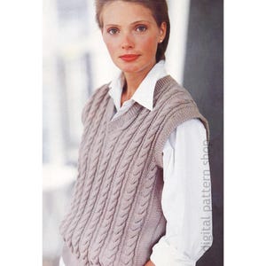 Könnte beinhalten: Eine hellbraune Strickweste mit Zopfmuster und V-Ausschnitt, getragen über einem weißen Hemd mit Kragen. Die Weste hat ein strukturiertes, vertikales Zopfmuster. Das Bild ist eine Studioaufnahme, mit dem Text "digital pattern shop".