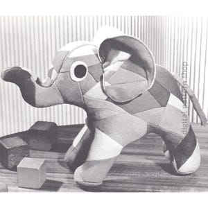 May include: A black and white patchwork elephant toy with a large eye. The elephant is standing on a wooden surface with wooden blocks.