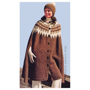 May include: A brown knitted cape with a white and brown geometric pattern around the neck. The cape has a button closure and is worn with a white knit hat.