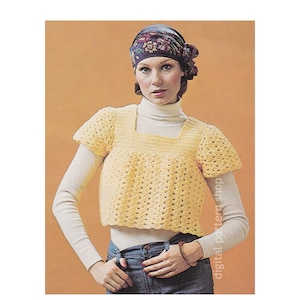 Può includere: Un top di uncinetto giallo con scollo quadrato e maniche corte. Il top è indossato sopra un dolcevita bianco e jeans blu. La modella indossa un foulard con motivo floreale.