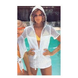 May include: White crochet hooded cover-up with a tie belt. The cover-up has a loose fit and short sleeves. The model is wearing the cover-up over a yellow swimsuit.