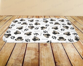 May include: White rectangular dog bed with a repeating pattern of pug faces, paw prints, and bone shapes. The pug faces are brown and black, the paw prints are gray, and the bones are light gray.