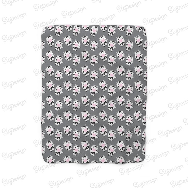May include: A gray fabric baby blanket with a repeating pattern of black and white cows with pink noses.